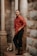 man in red dress shirt and black denim jeans sitting on concrete column