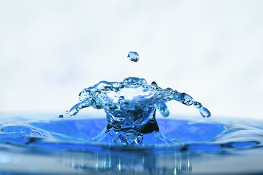 Close-up of a crystal-clear water droplet creating gentle ripples on a soft aqua blue background.
