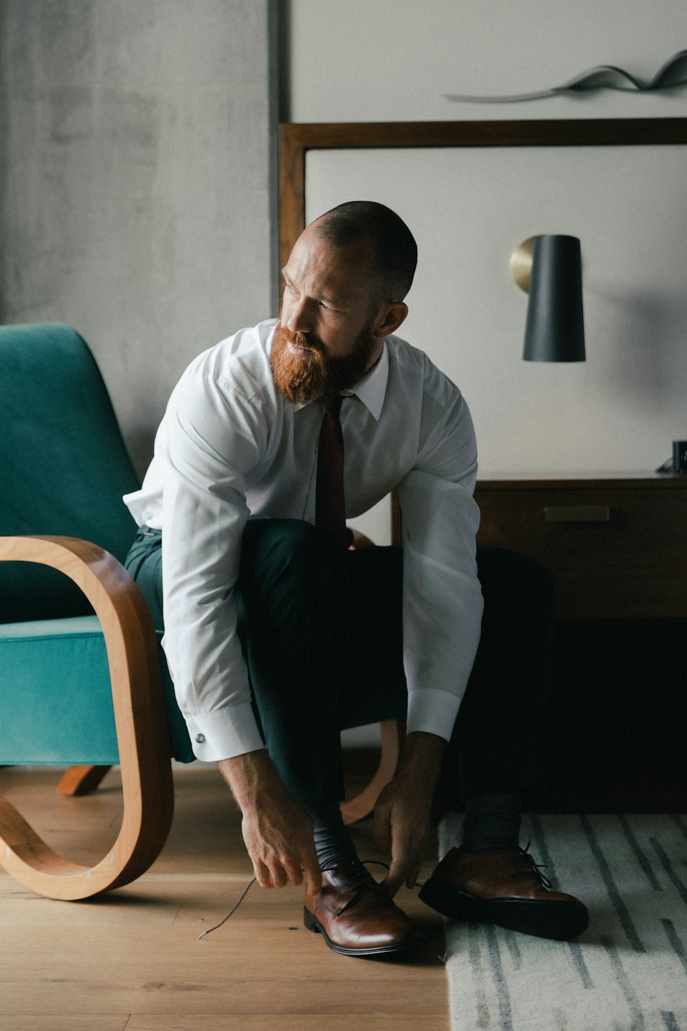 man in white dress shirt and black dress pants standing beside brown wooden chair