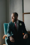 man in black suit sitting on blue sofa chair