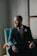 man in black suit sitting on blue sofa chair