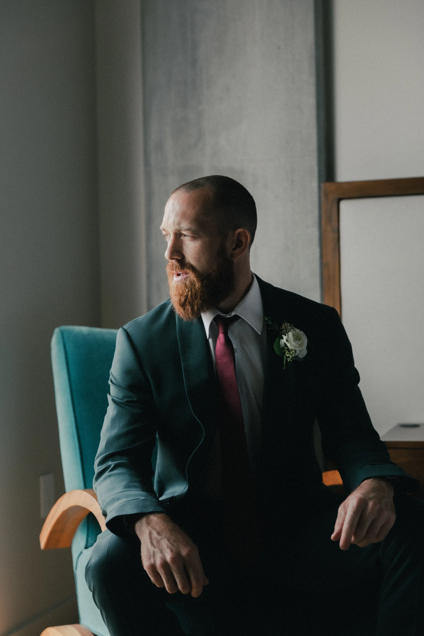Man in elegant tailored black suit seated in a refined interior setting, formal wedding portrait