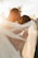 A couple is embracing intimately, with soft sunlight creating a warm, ethereal glow around them. The bride’s veil billows gracefully in the breeze, and both individuals have joyful, serene expressions as they share a close moment.