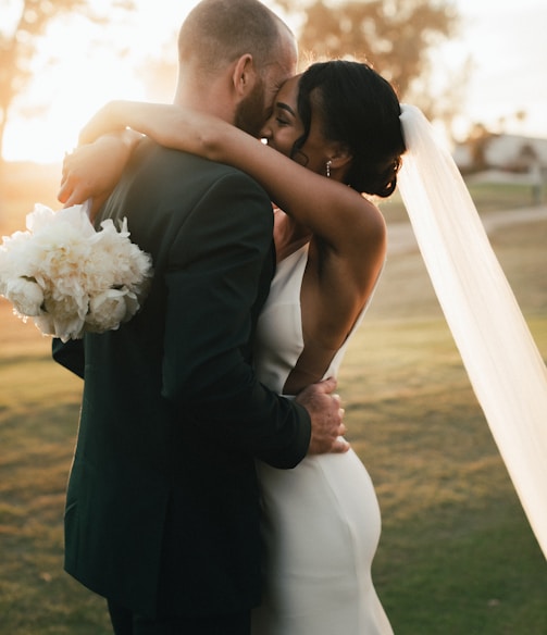 man in black suit kissing woman in white wedding dress