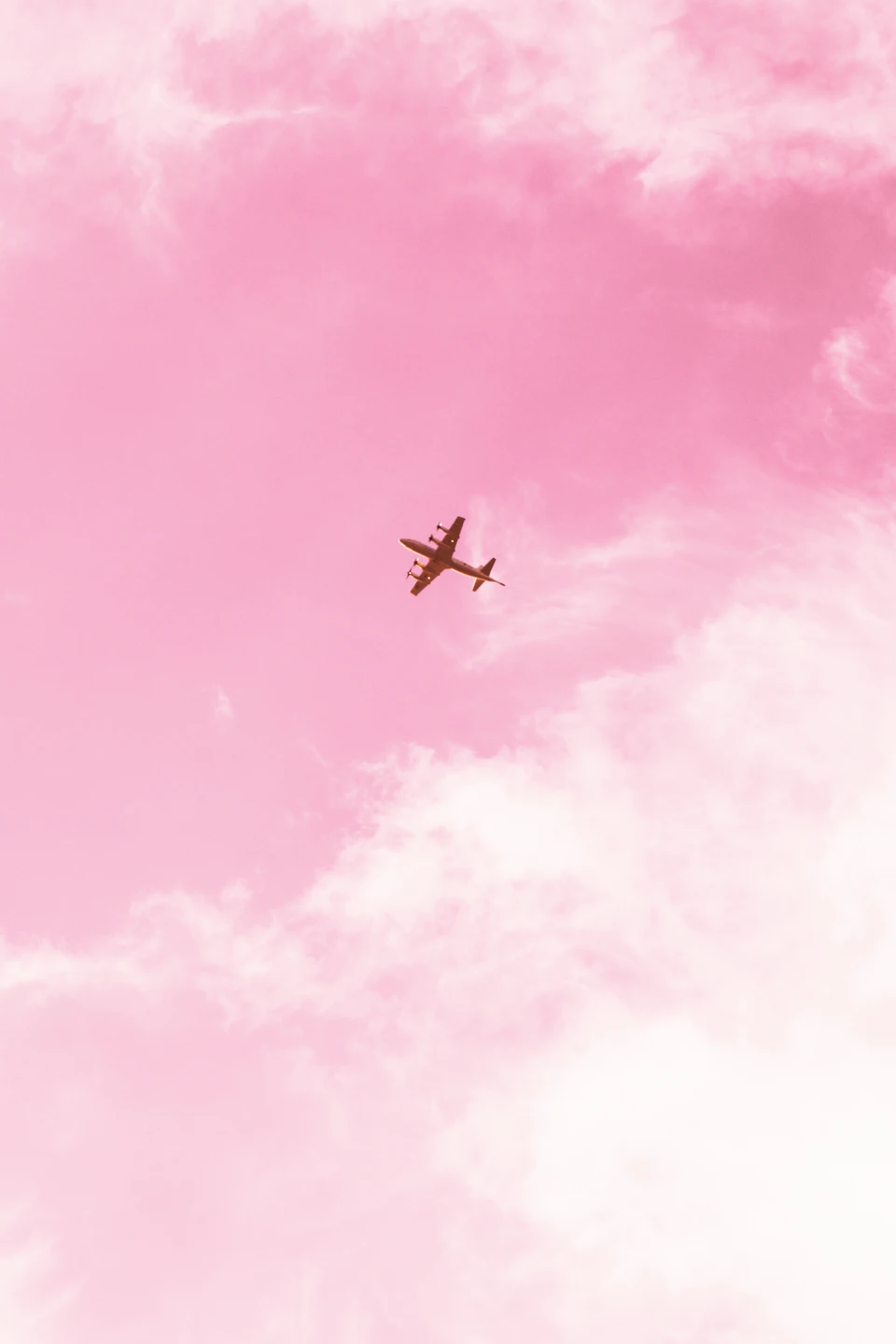 Small airplane soars through pink and white cloud-filled sky with central flight path