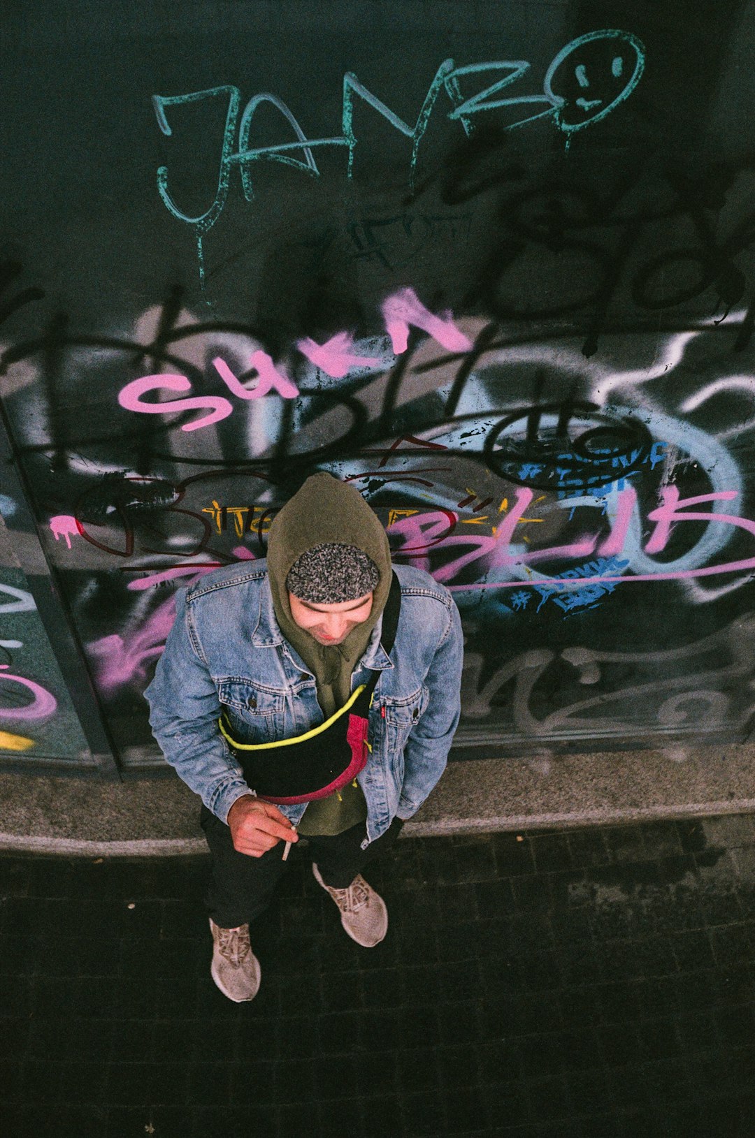 man in blue jacket and black pants sitting on concrete wall