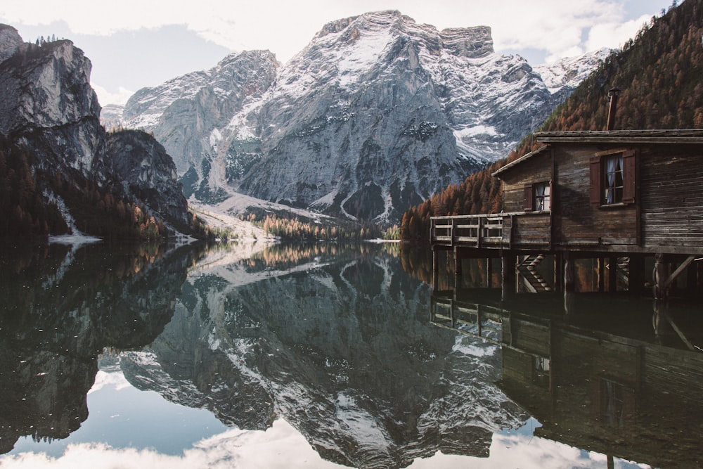 brown wooden house on lake near snow covered mountain