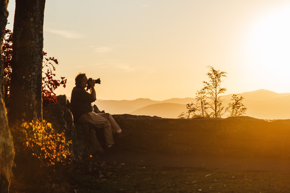 man and woman sitting on rock during sunset