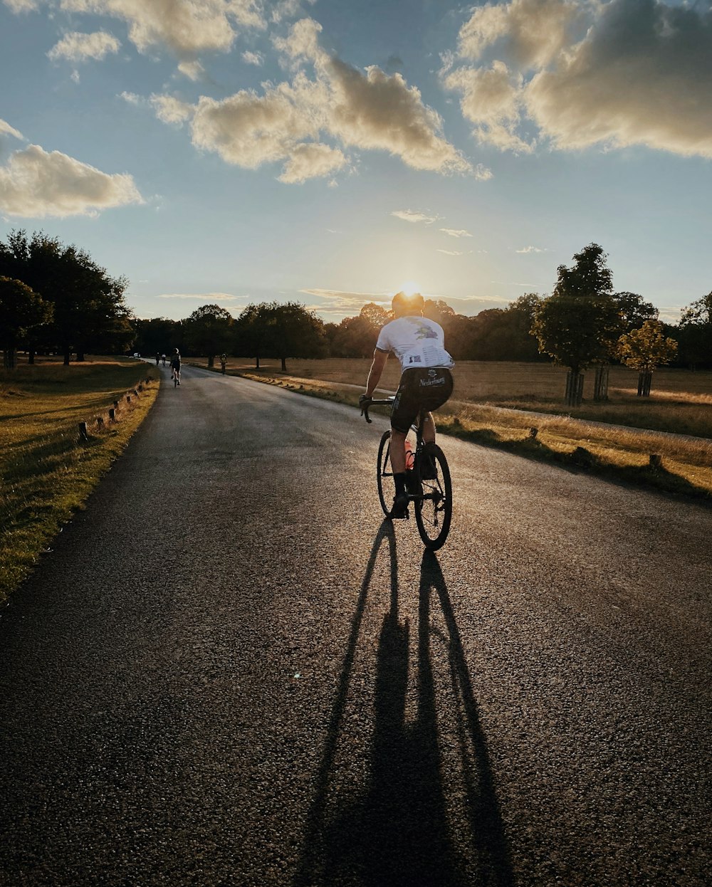 hombre con camisa blanca montando bicicleta en una carretera asfaltada gris durante el día