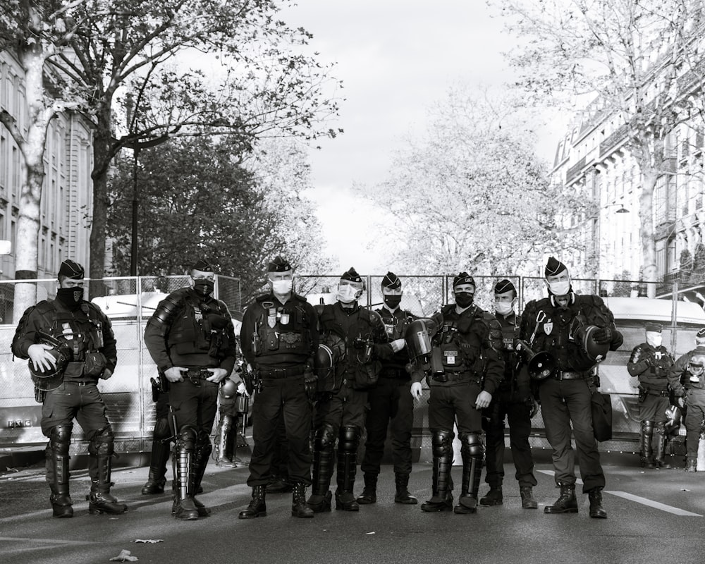 grayscale photo of men in black and white camouflage uniform standing on road