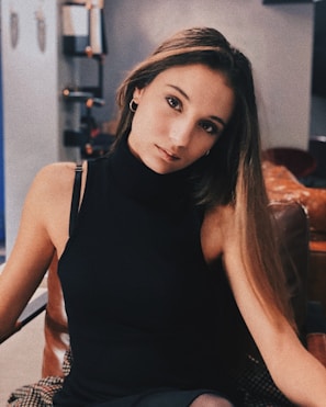 Seductive young Asian college girl escort sitting stylishly in a modern hotel room.