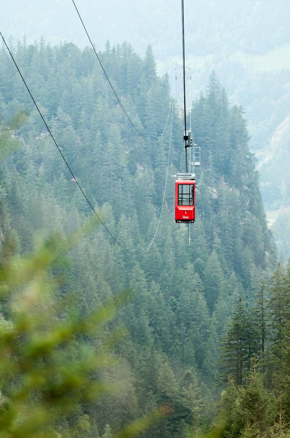 red cable car over green trees during daytime