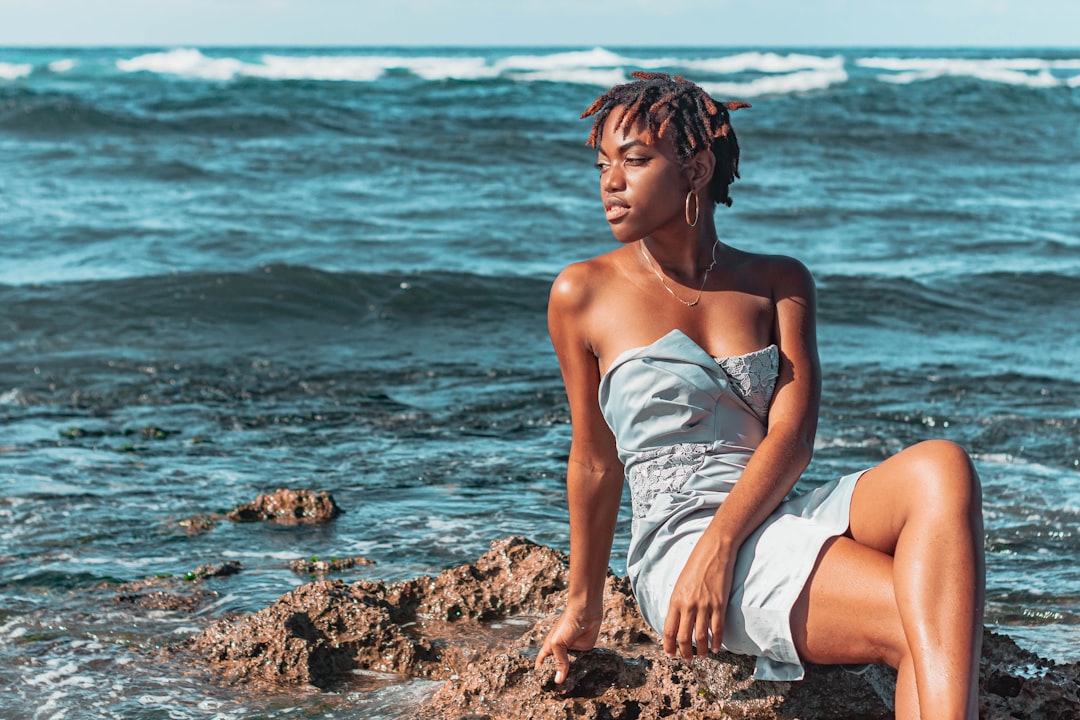 woman in white tube dress sitting on brown rock near body of water during daytime