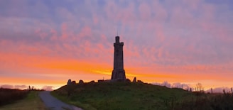 A repaired tower standing strong on a hilltop with a sunset backdrop.