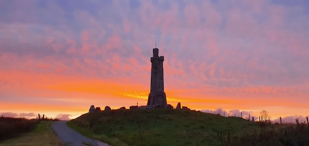 A repaired tower standing strong on a hilltop with a sunset backdrop.