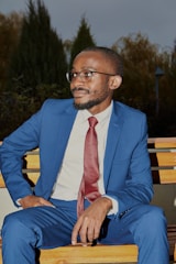 man in blue suit sitting on brown wooden bench