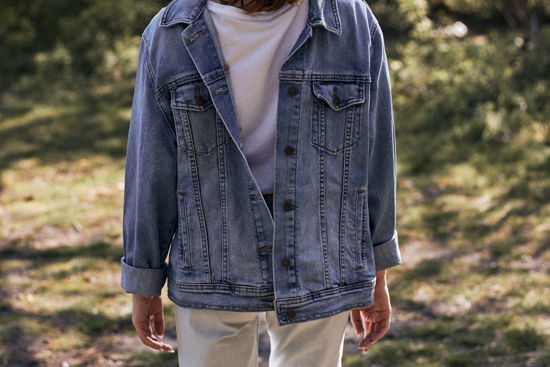 man in blue denim jacket and white pants standing on green grass field during daytime