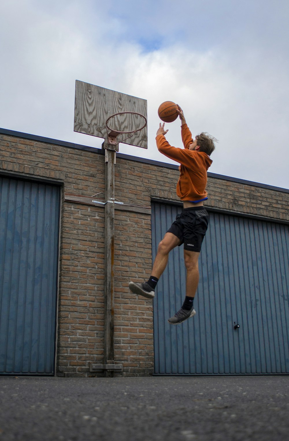 Hombre con camisa naranja y pantalones cortos negros jugando baloncesto