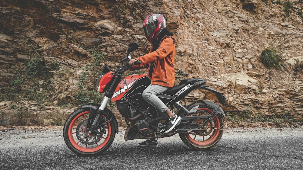 man in orange jacket riding black and red sports bike