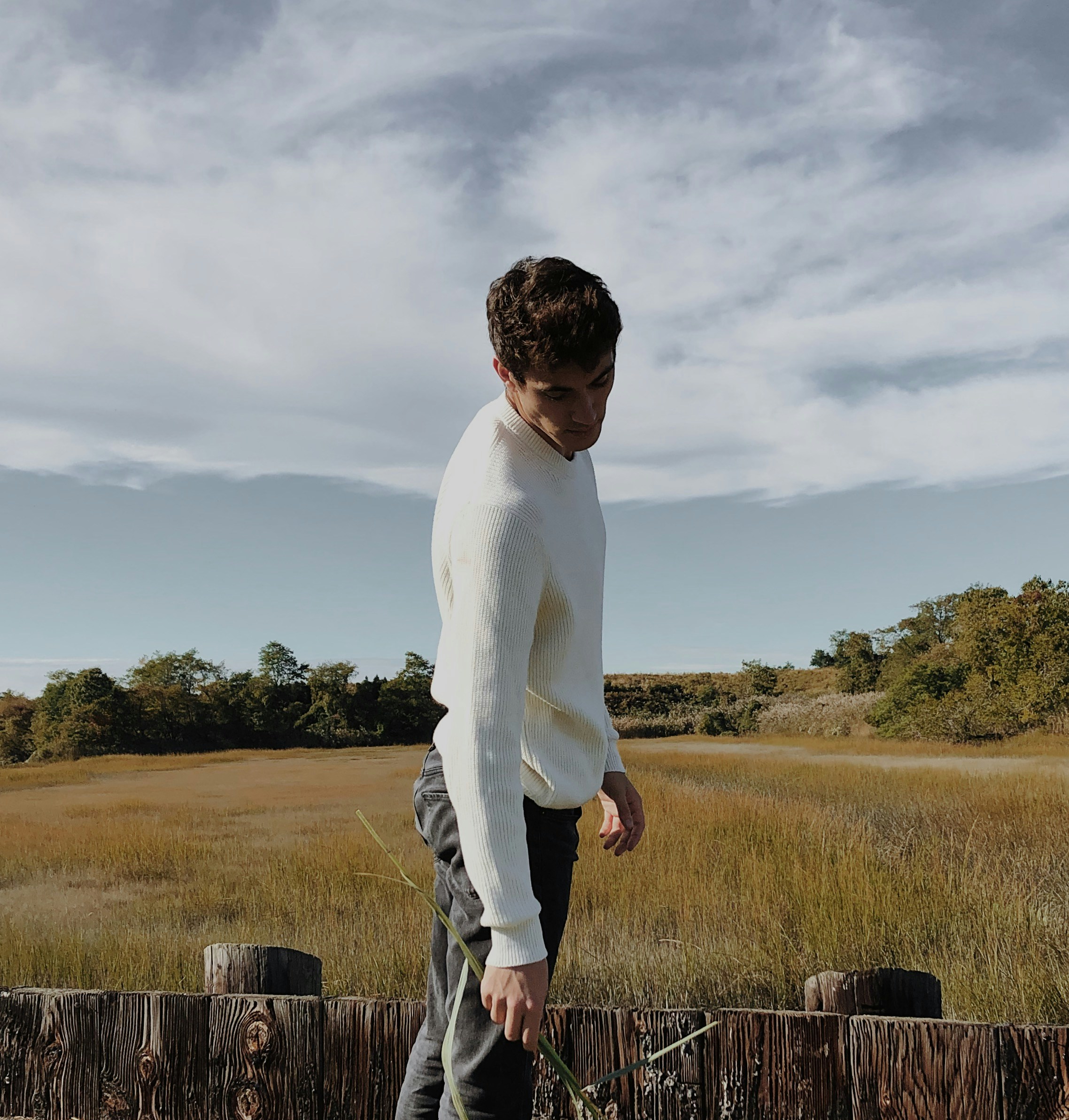 man in white long sleeve shirt and gray pants standing on brown wooden fence during daytime