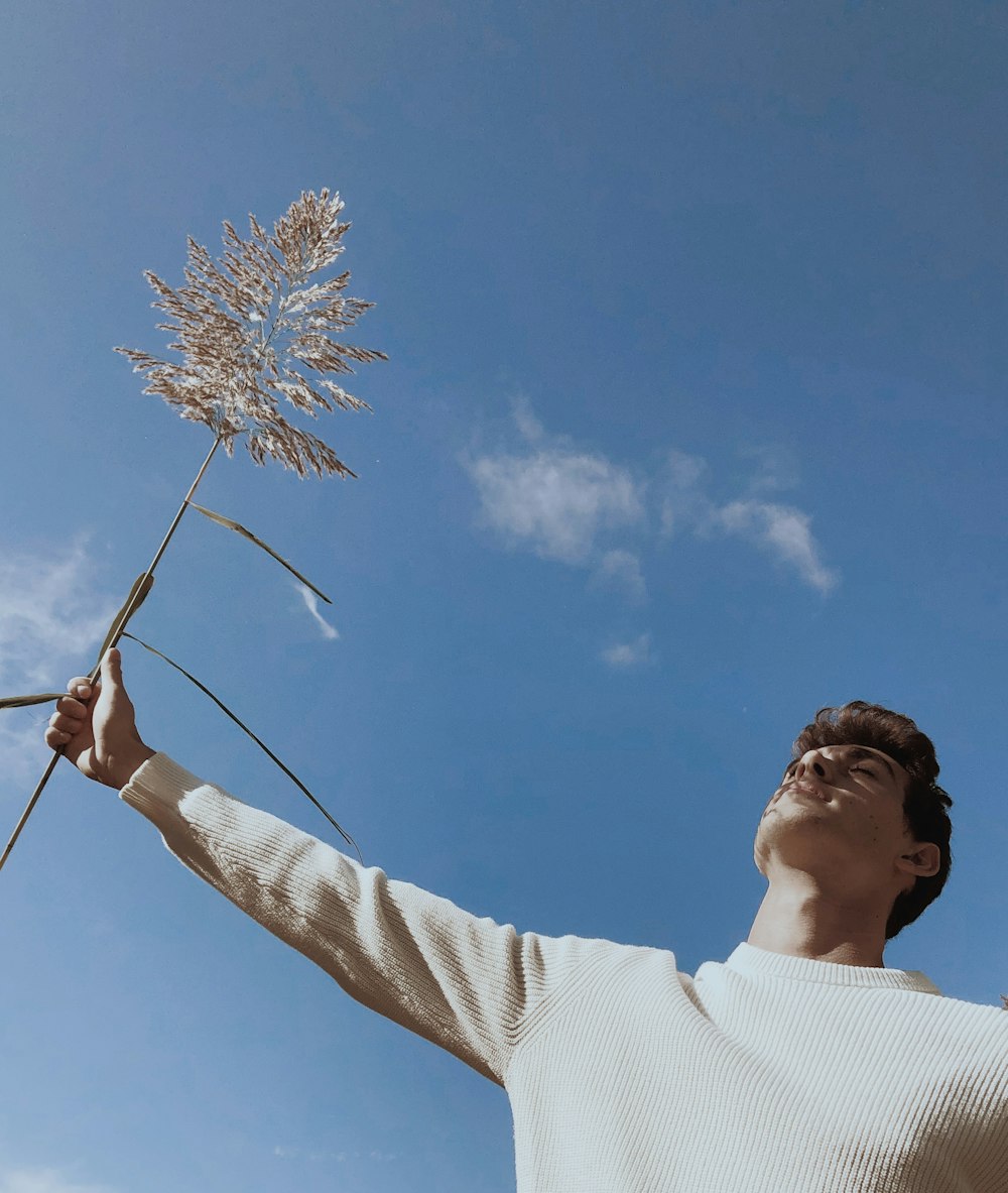 昼間の青空の下で茶色と白の花を手にした白いセーターの男性