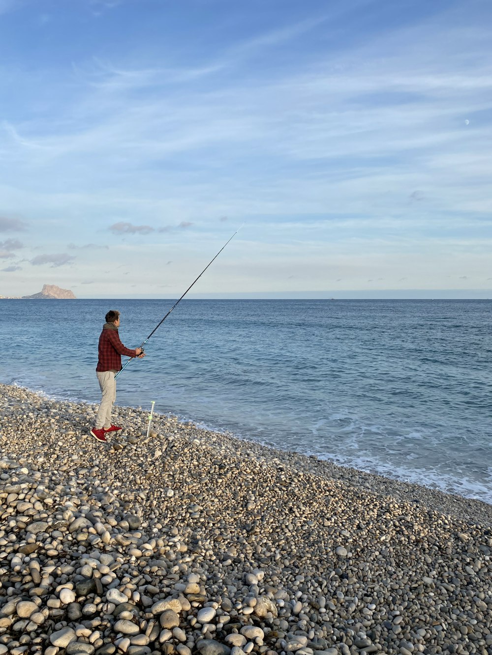 woman in red jacket and white pants fishing on sea during daytime