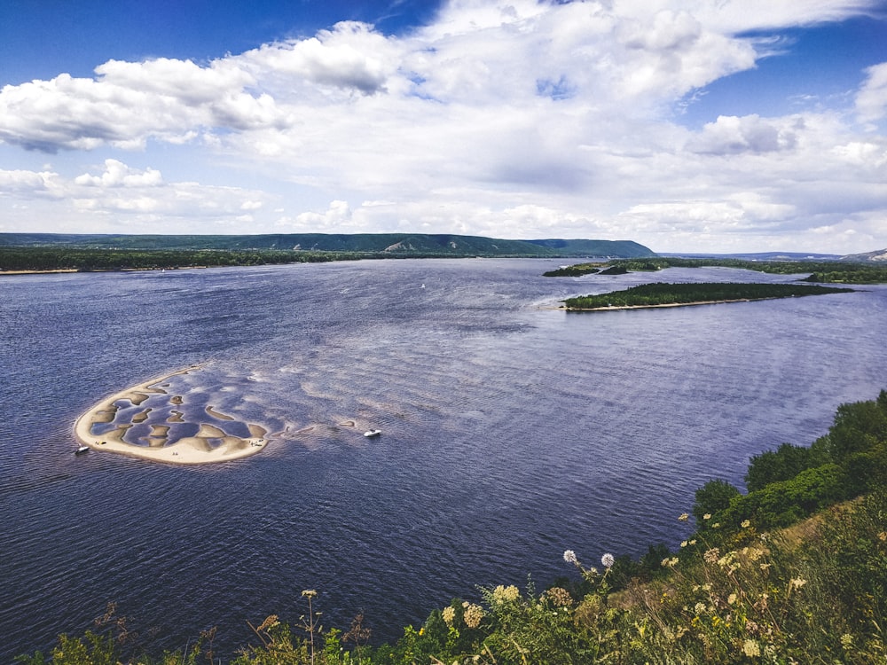 campo de grama verde perto do corpo de água sob nuvens brancas e céu azul durante o dia