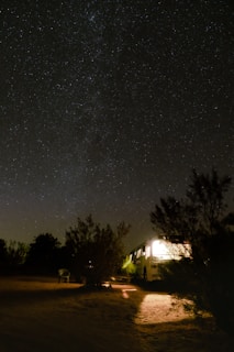 A cozy campfire glowing under a starry night sky beside a vintage RV parked on a quiet forest clearing.