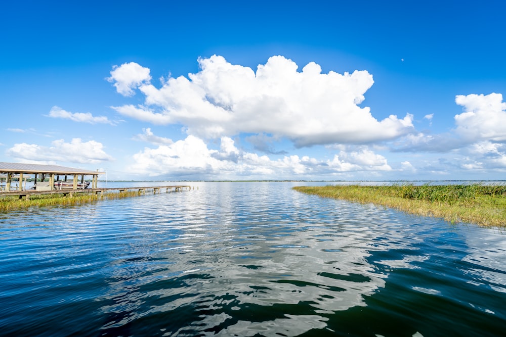 green grass field beside body of water under blue sky and white clouds during daytime