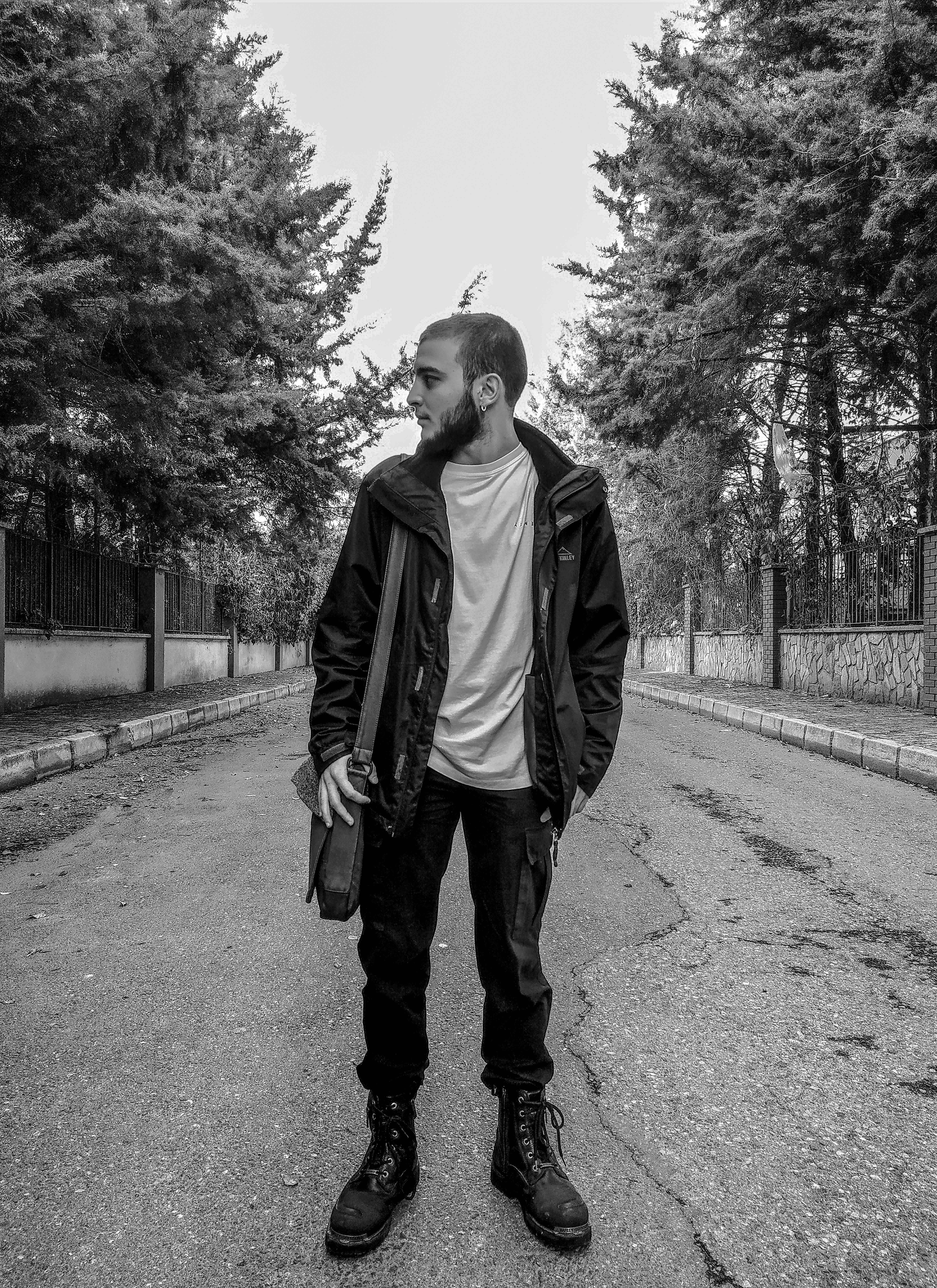man in black jacket and black pants standing on road in grayscale photography