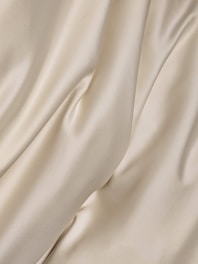 A soft beige fabric draped elegantly over a cream background, highlighting texture and quality.