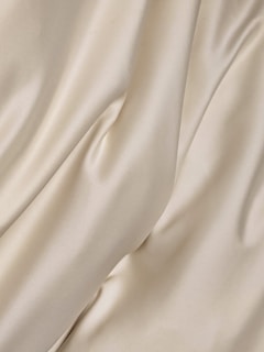 Cream-colored fabric with soft folds and a smooth texture creates a gentle flow across the surface.