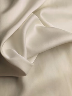 A smooth, flowing piece of light cream-colored fabric with soft folds and a silky texture.