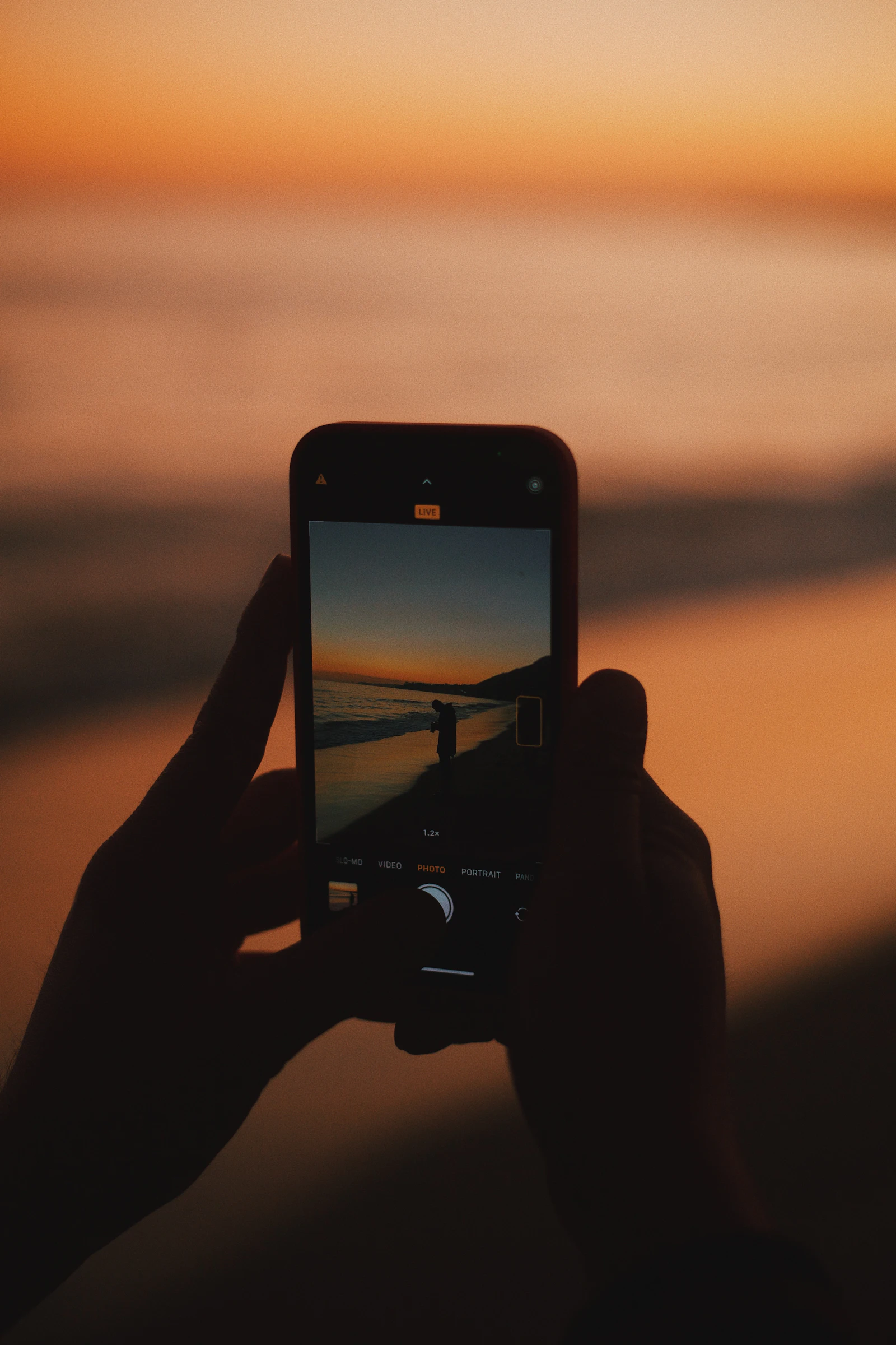 Traveller holding a phone with an eSIM data connection while photographing a sunset over the water