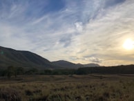 Sunset view over rolling hills with vibrant green fields in the foreground.