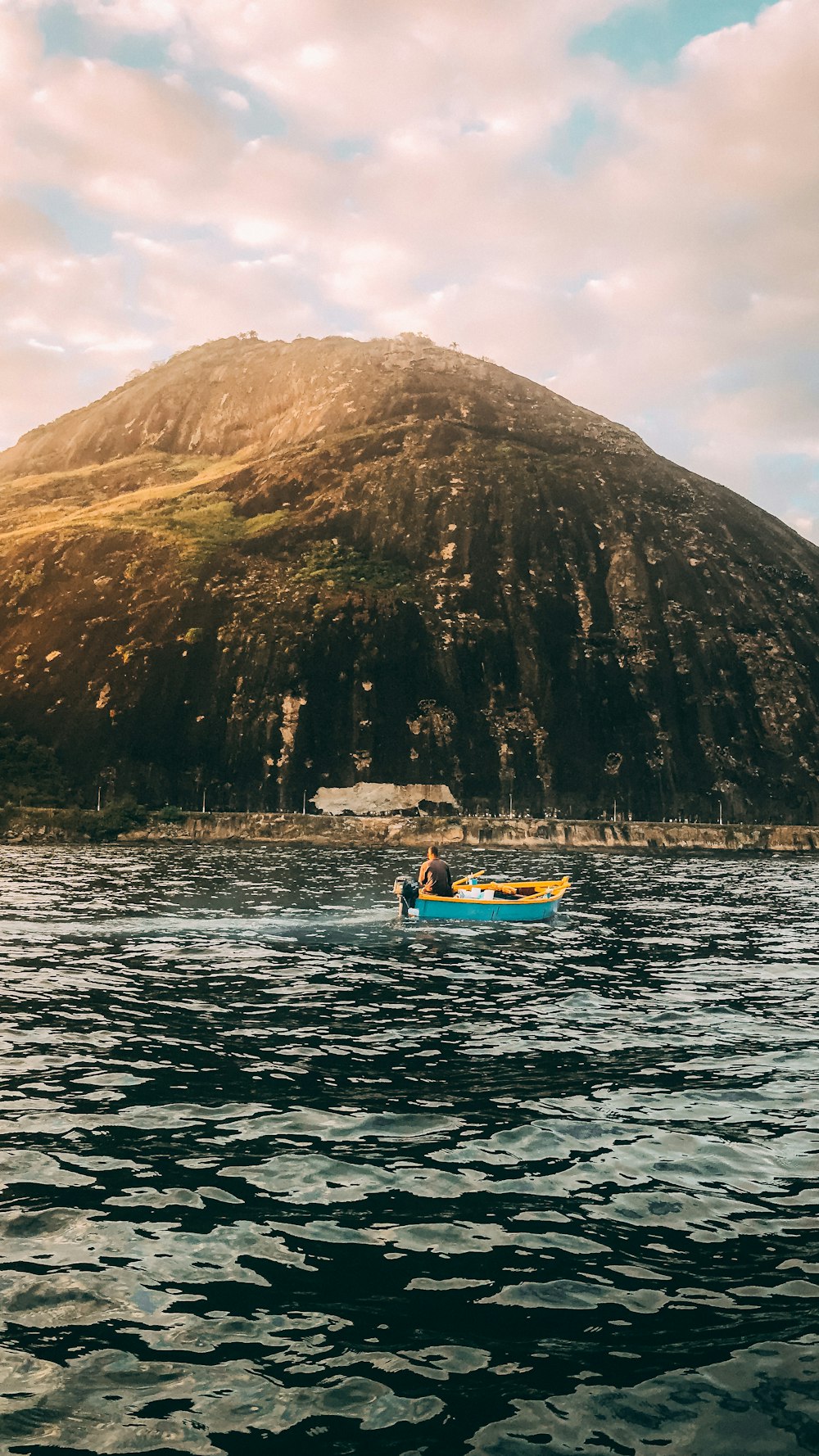 blue and yellow boat on water near brown mountain during daytime