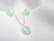 A set of jewelry featuring a necklace and matching earrings, each adorned with light blue gemstones encircled by small silver embellishments, displayed on a textured white fabric background.