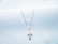 A delicate silver necklace with a cross-shaped pendant, resting on a soft white textured fabric. The pendant is studded with small sparkling stones, adding a touch of elegance.