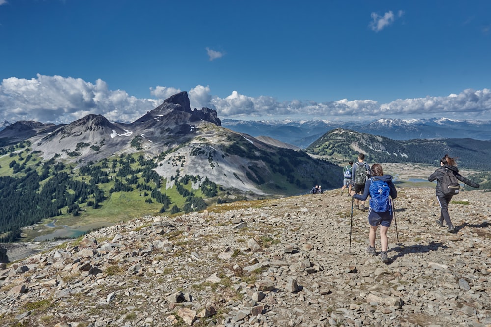 man in blue shirt and blue shorts walking on rocky ground near mountain under blue sky