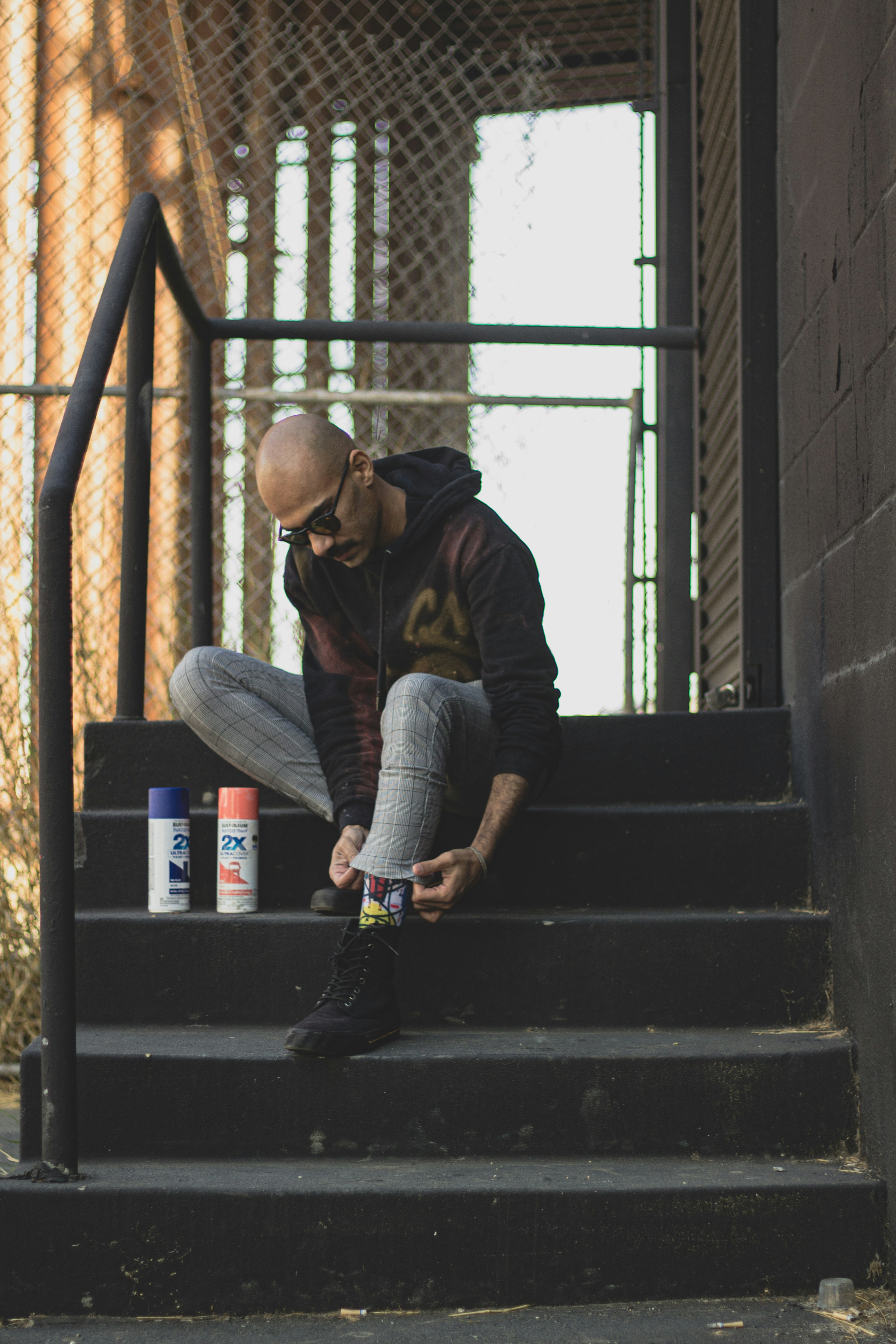 man in black jacket and gray denim jeans sitting on black metal staircase