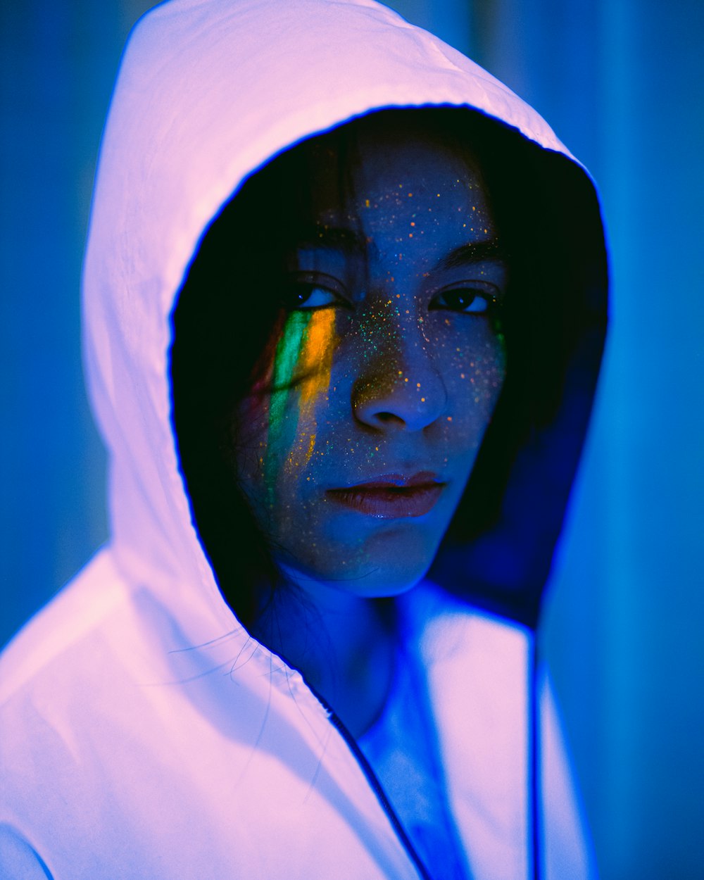 man in white hoodie with blue green and yellow face paint