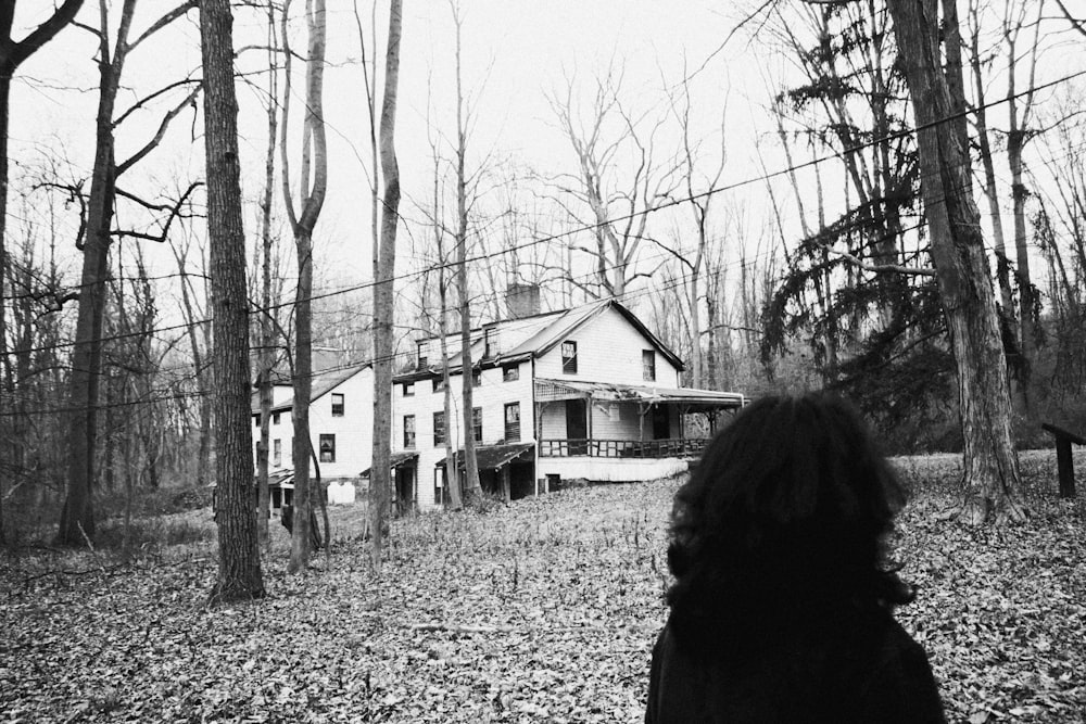 foto em tons de cinza da mulher no casaco preto em pé perto de árvores nuas