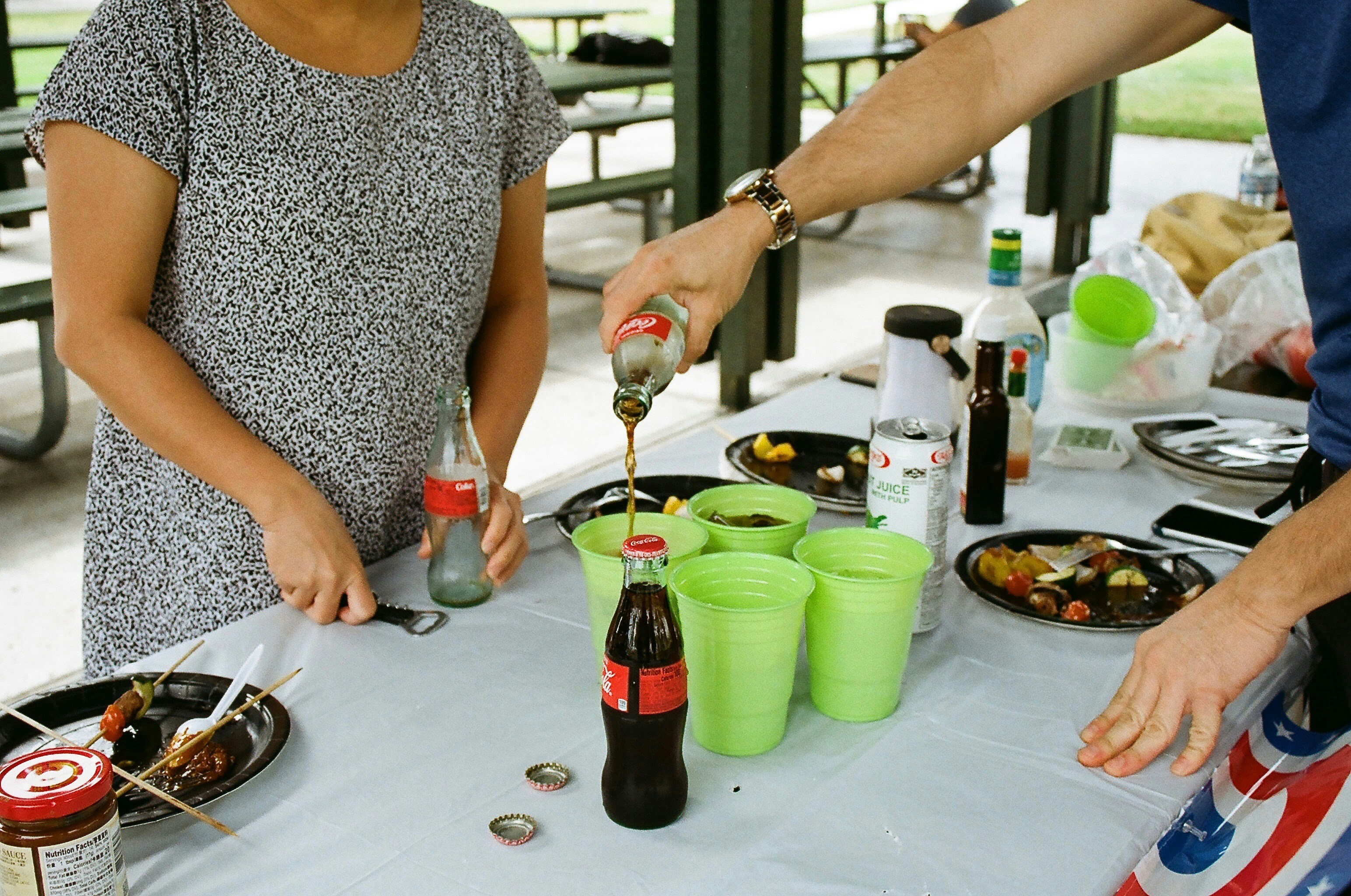 two people pouring coke into green disposable cups
