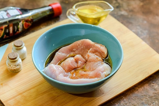 Close-up of marinated chicken cuts ready for cooking with spices in the background.