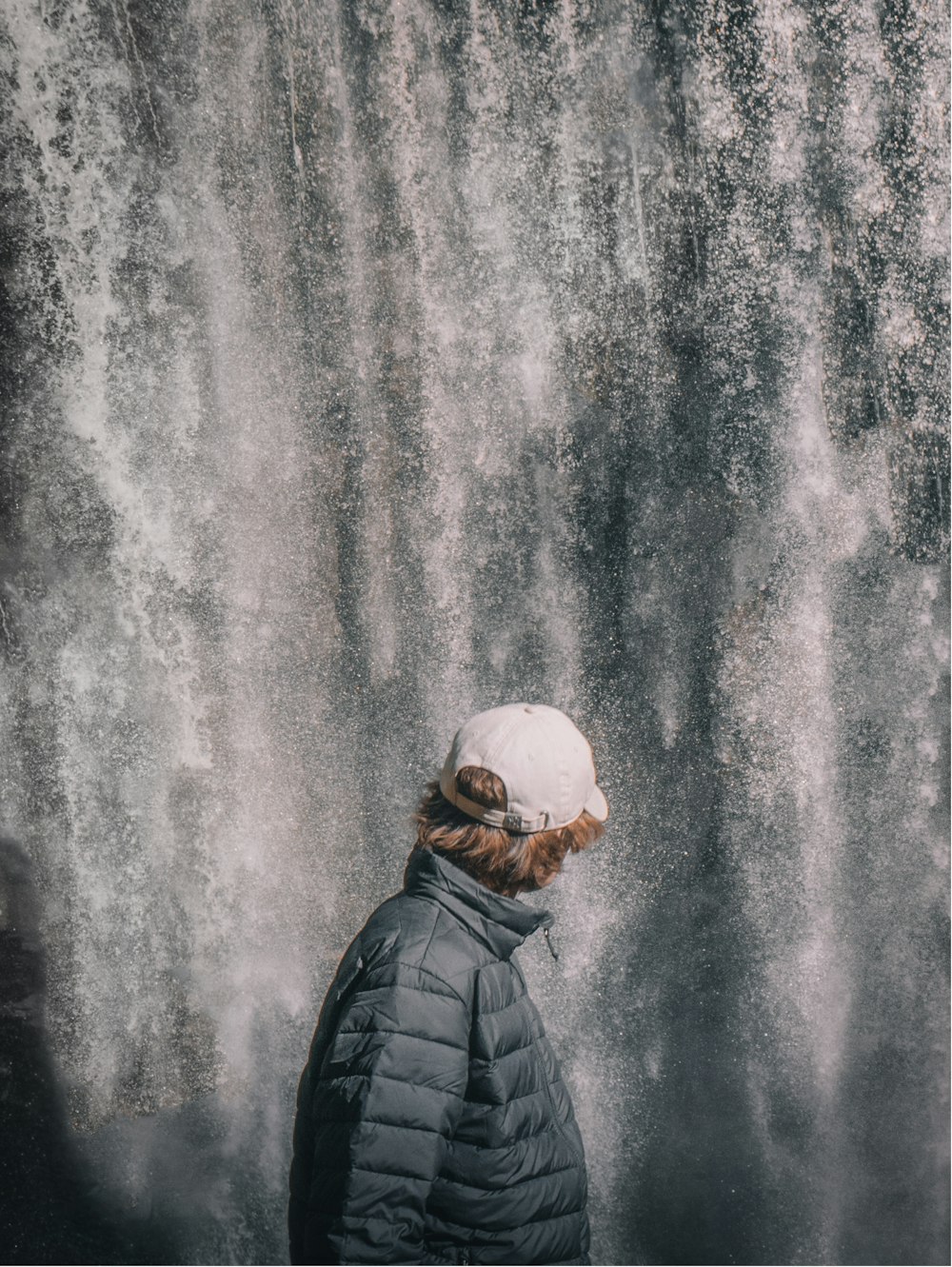 man in black leather jacket standing in front of water falls