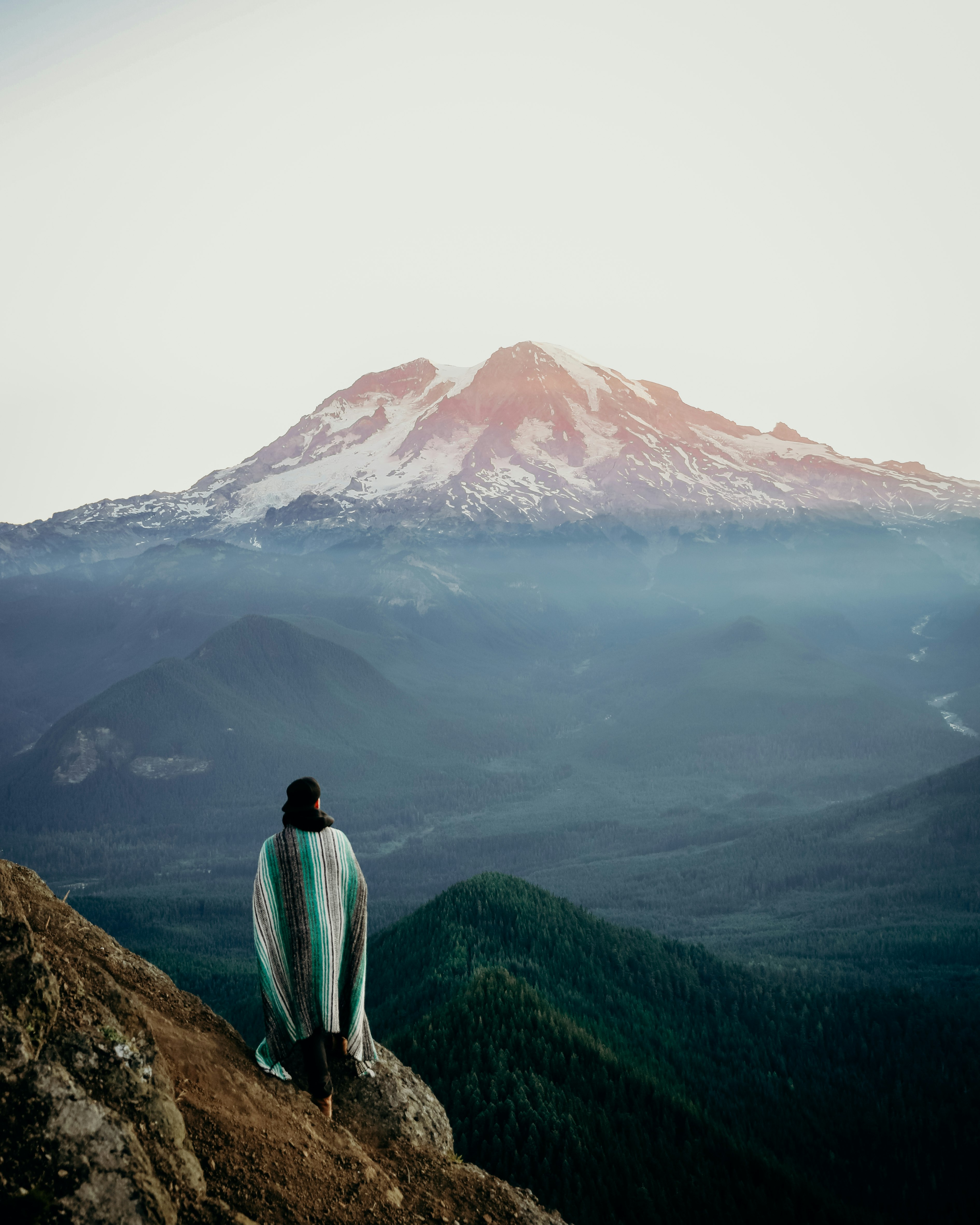 man in green shirt standing on brown rock near mountain during daytime