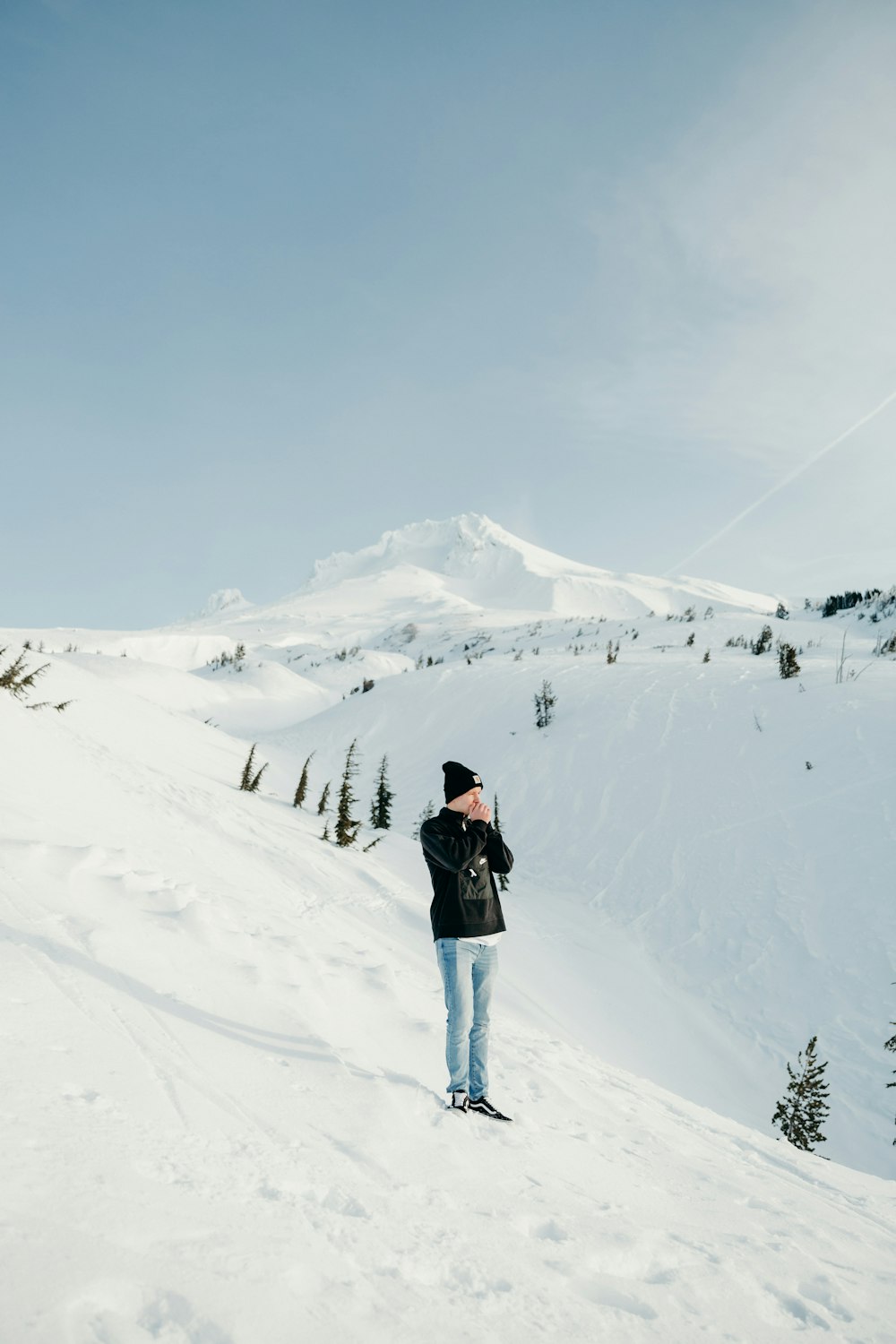 昼間、雪に覆われた山に立つ黒いジャケットとブルーデニムジーンズの男性