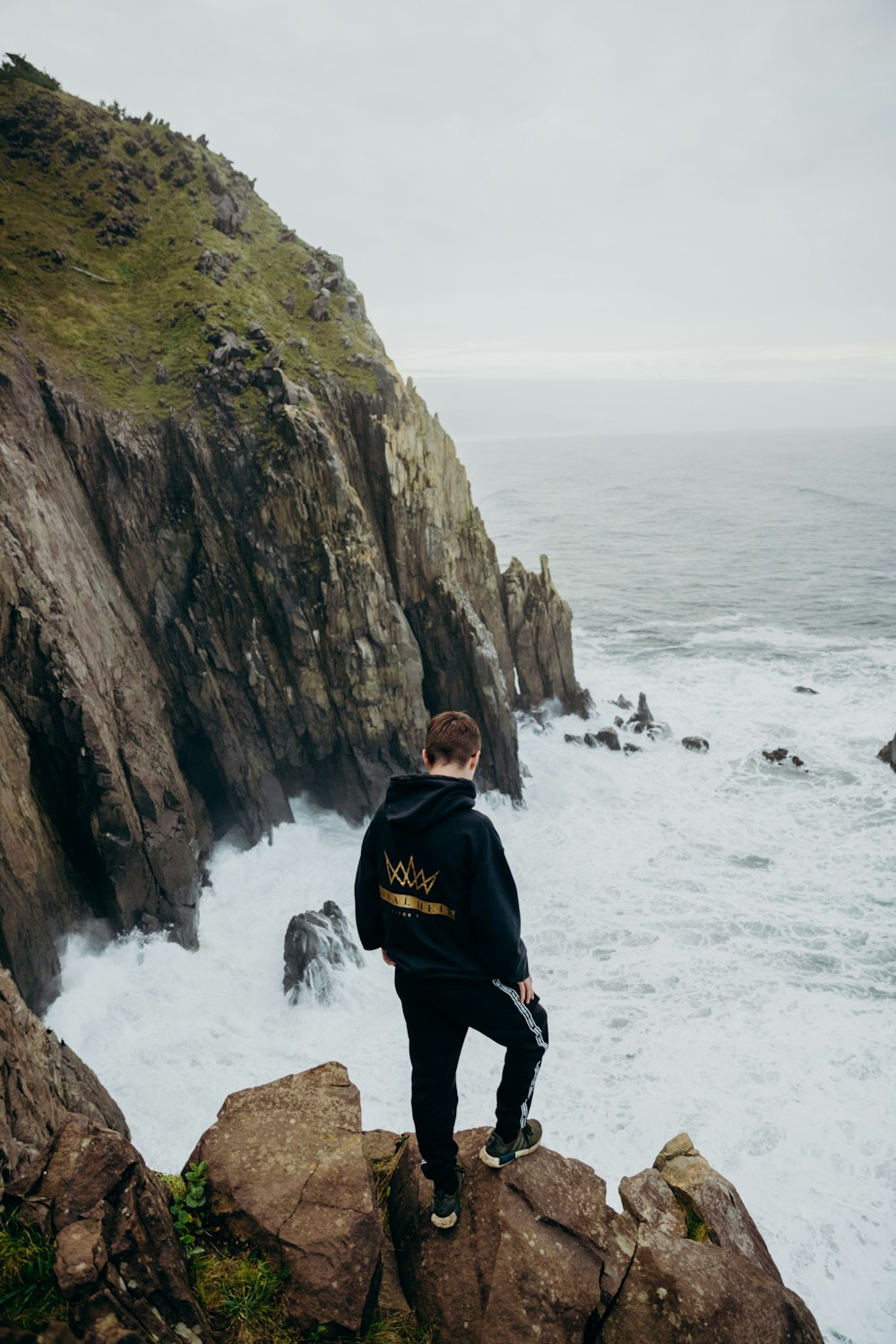 낮 동안 수역 근처의 암석에 서 있는 검은 재킷을 입은 남자