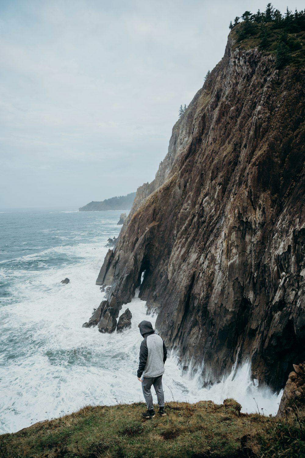 man in gray jacket standing on brown rock formation near body of water during daytime