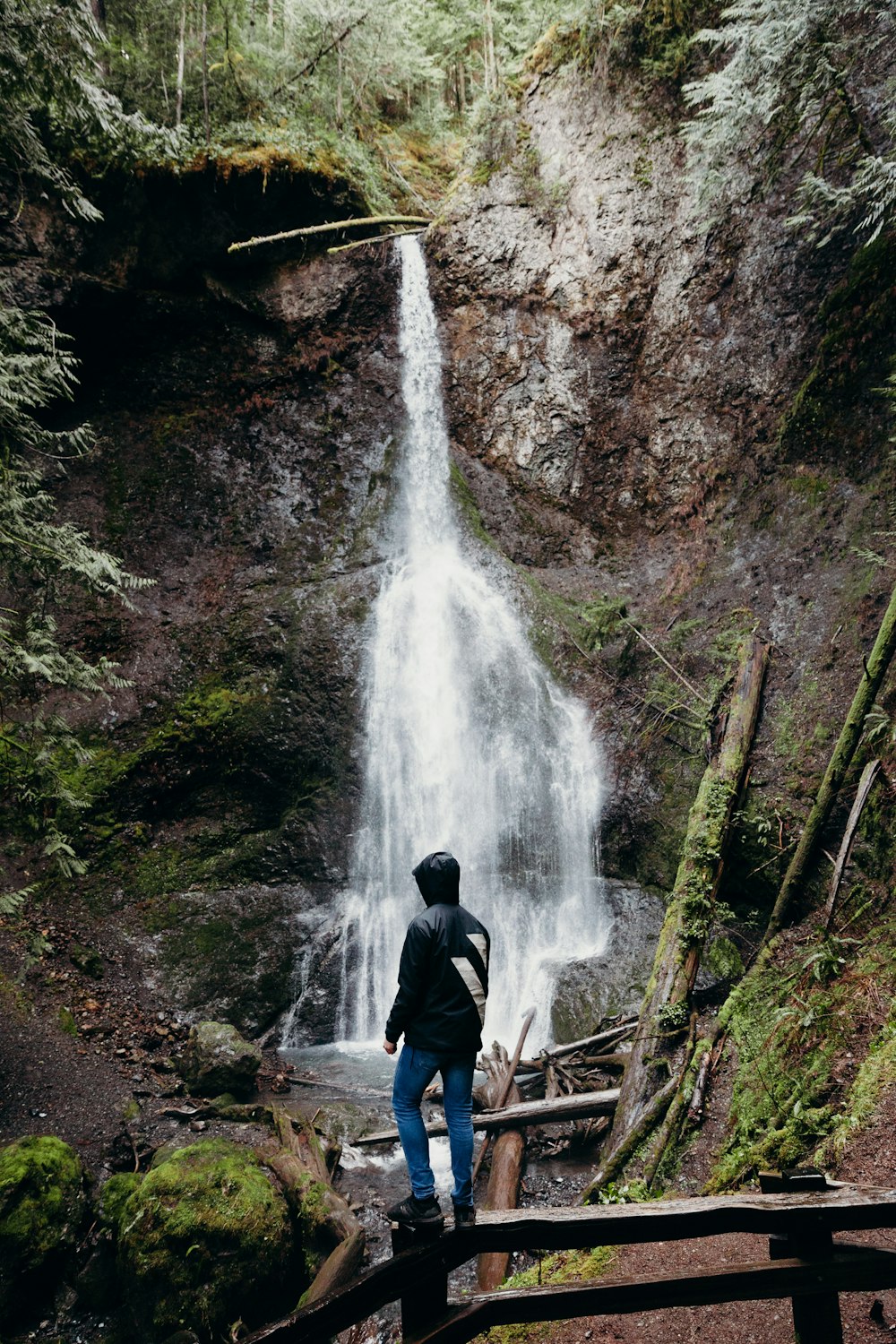 man in black jacket standing in front of waterfalls during daytime